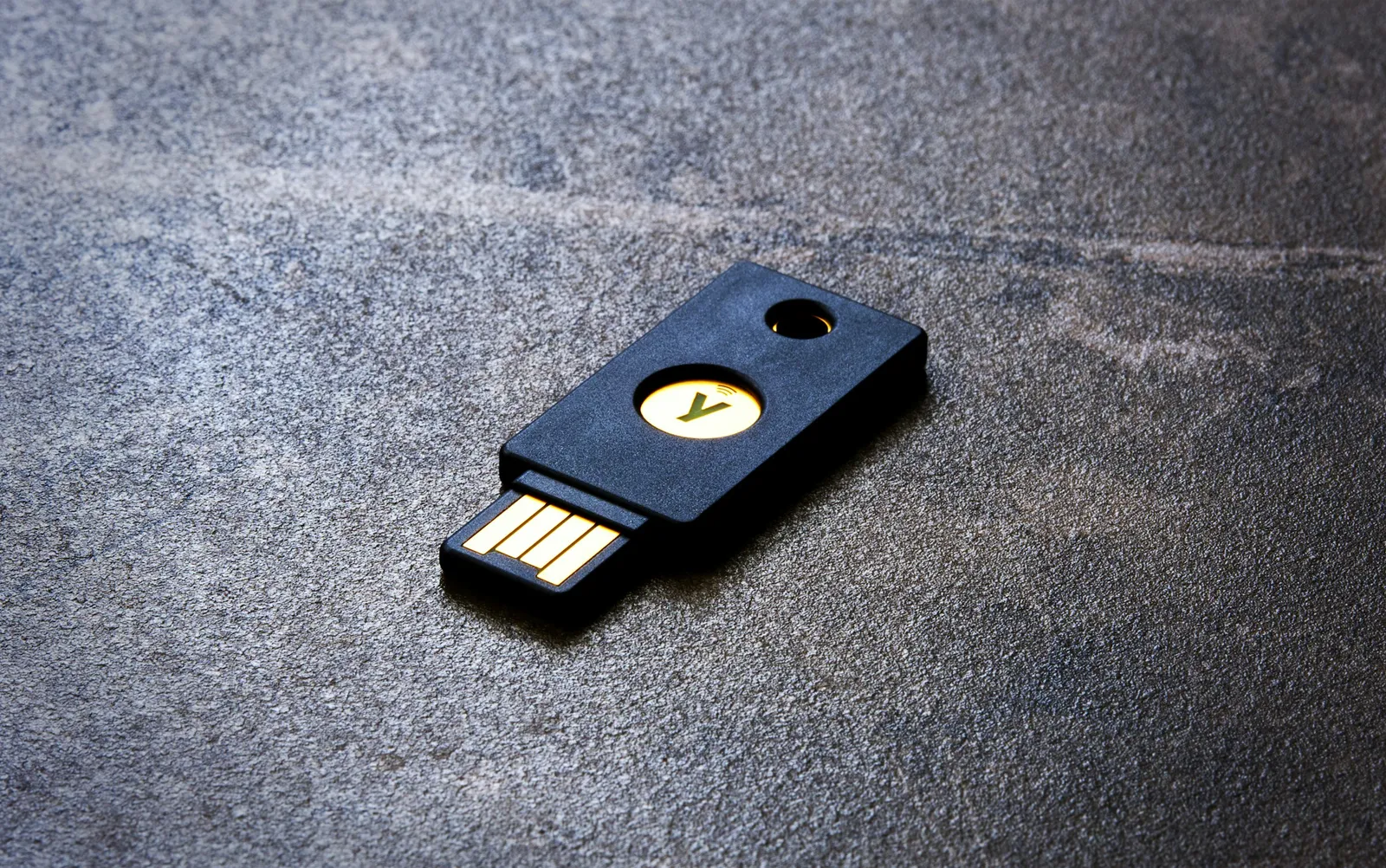 Sprzętowy klucz bezpieczeństwa USB do uwierzytelniania wieloskładnikowego leżący na ciemnym kamiennym blacie