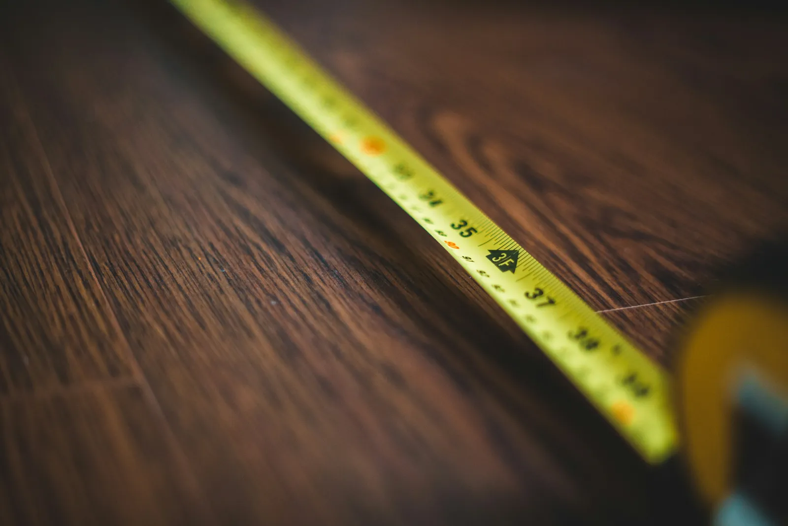 Rozwinięta żółta miarka stolarska leżąca ukośnie na ciemnym drewnianym blacie