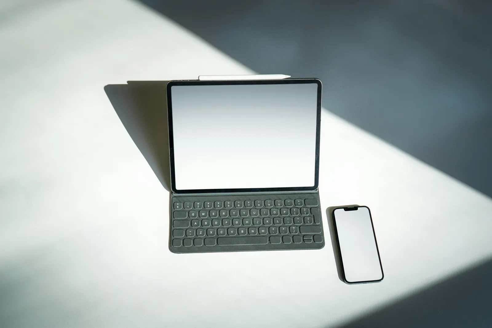 Tablet z klawiaturą i smartfon z wygaszonymi ekranami na jasnym blacie w smudze światła